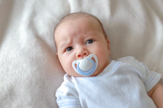 Headshot portrait of cute newborn baby lying on bed with pacifier on mouth. Mixed race Asian-German ...