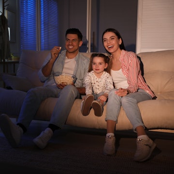 Family watching movie with popcorn on sofa at night, space for text