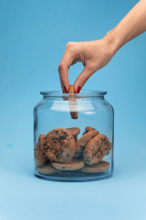Shot of a woman hand taking cookies from a glass jar on blue background.
