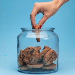 Shot of a woman hand taking cookies from a glass jar on blue background.