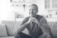 cheerful senior man smiles, sitting on sofa couch in living room
