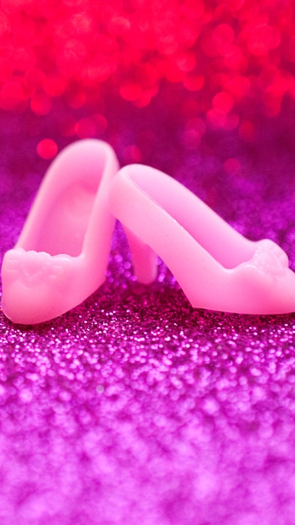Pair of pink high heel doll shoes on pink glitter background 