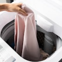 Hands of young woman putting  clothe into washing machine at condominium. Laundry concept. Top view