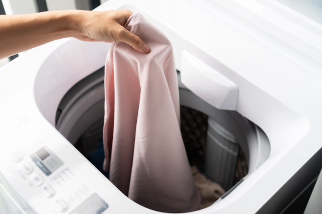 Hands of young woman putting clothe into washing machine at condominium. Laundry concept. Top view