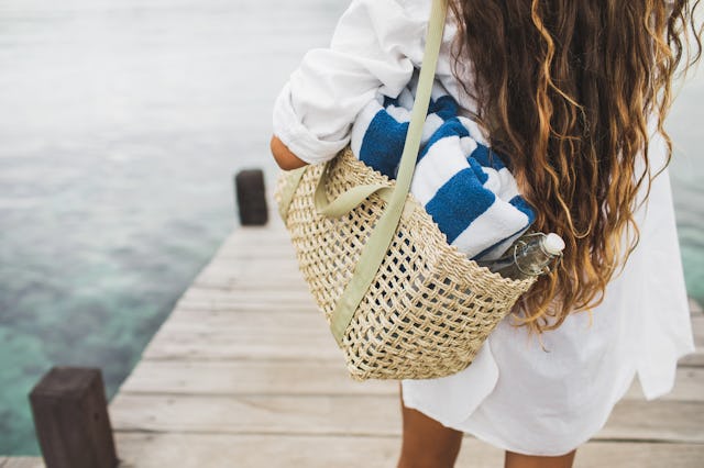 Woman with handmade wicker bag, two beach towels and glass bottle for water going to the beach. View...