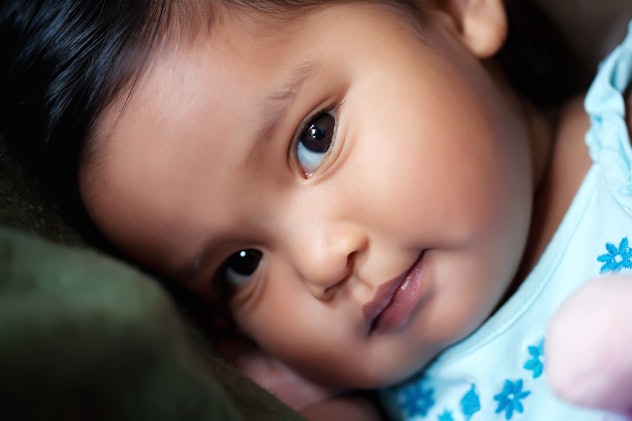 baby girl resting her head on a pillow, with a subtle smile in an article about baby girl names that...