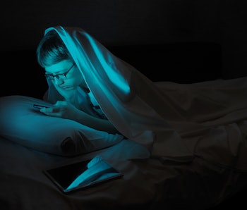 Afflicted Teenager in bed with a gadget. 