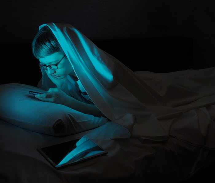 Afflicted Teenager in bed with a gadget.