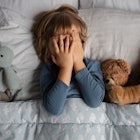 一个孩子躺在床上，周围都是毛绒玩具，还捂着他们的脸