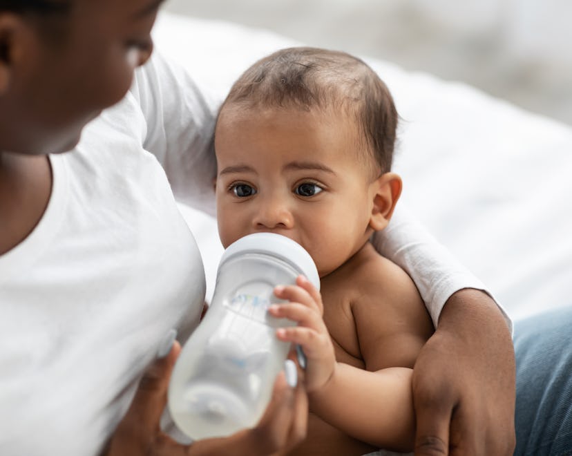 Childcare Concept. Closeup portrait of happy African American woman holding baby bottle and feeding ...