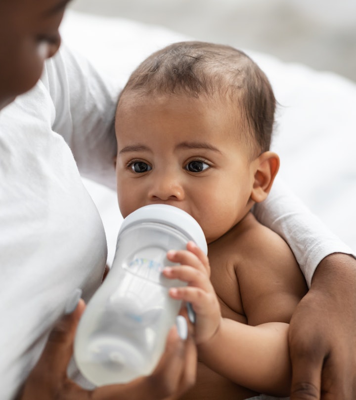 Childcare Concept. Closeup portrait of happy African American woman holding baby bottle and feeding ...