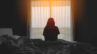 silhouette of woman sitting on the bed next to the windows with sunlight in the morning in an article...