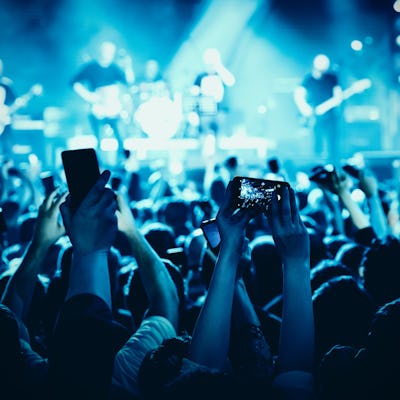 A lot of hands with the smartphone turned on to record or take pictures during the live concert