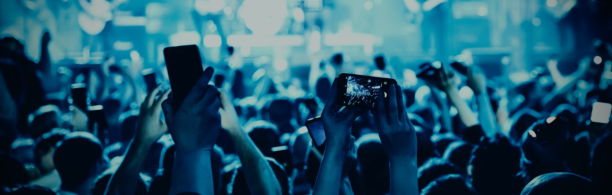 A lot of hands with the smartphone turned on to record or take pictures during the live concert