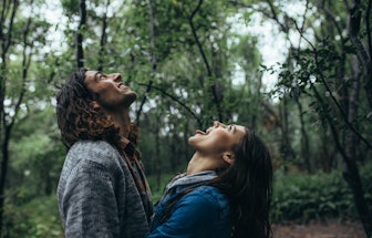 Couple catching raindrops on tongue on a rainy day at forest. Happy man and woman enjoying in a rain...