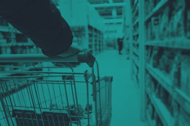 A man with a basket walks in a supermarket. Hand and part of the basket in focus, blurred background