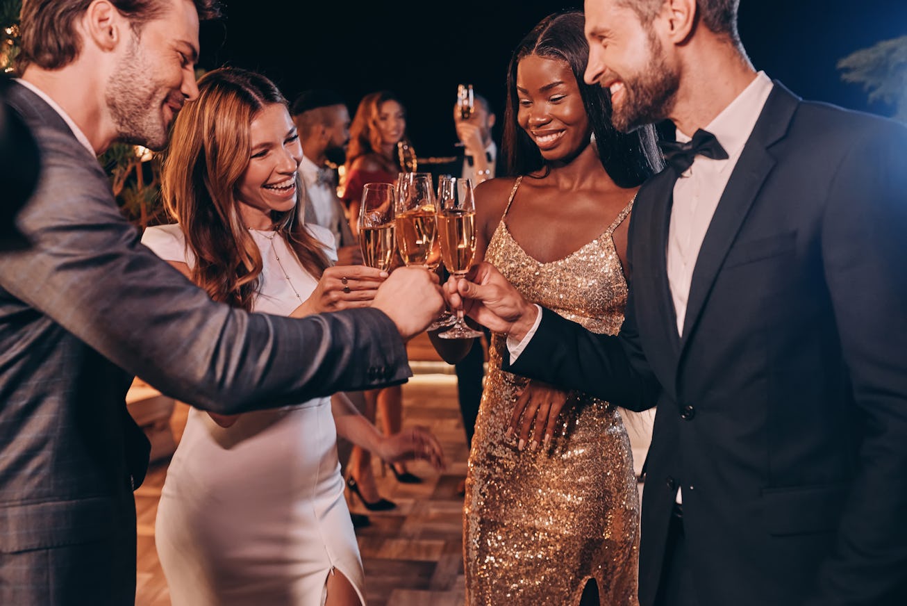 Group of people in formalwear toasting with champagne and smiling while spending time on luxury part...