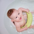 Toddler baby plays with a yellow duck toy while bathing. A happy infant child bathes in water while ...