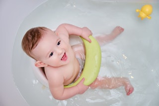 Toddler baby plays with a yellow duck toy while bathing. A happy infant child bathes in water while ...