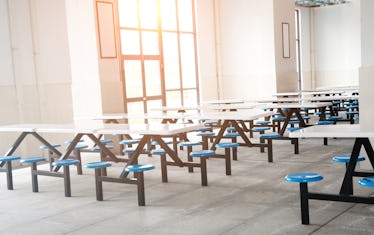 Clean school cafeteria with many empty seats and tables.