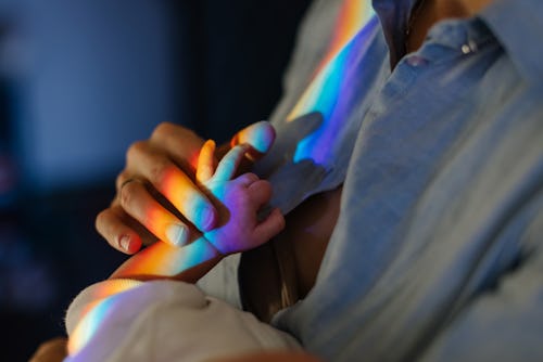 Mom holds baby by the hand in a spectrum rainbow in an article about rainbow baby announcement ideas