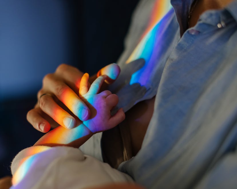 Mom holds baby by the hand in a spectrum rainbow in an article about rainbow baby announcement ideas