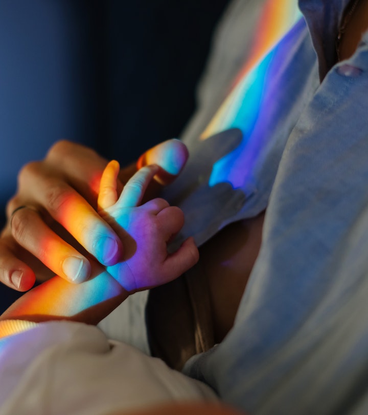 Mom holds baby by the hand in a spectrum rainbow in an article about rainbow baby announcement ideas