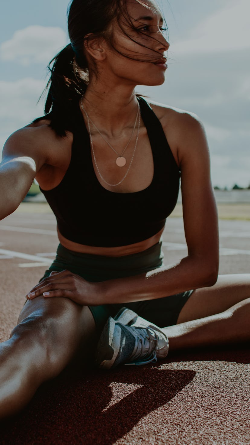 Athlete doing stretching exercises on running track. Woman runner stretching leg muscles by touching...
