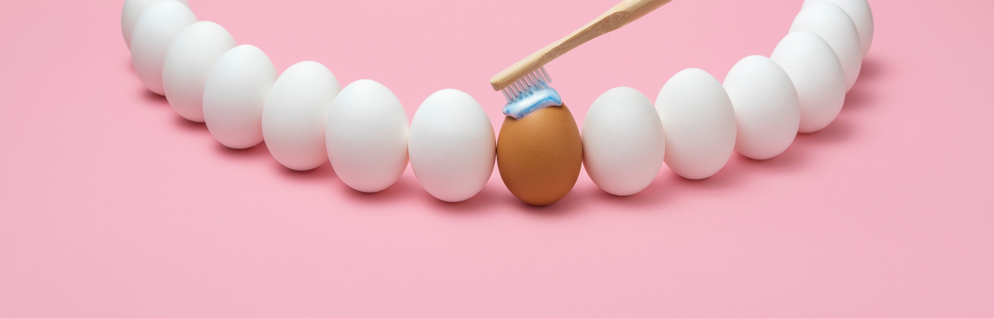 Concept for oral hygiene with a wooden toothbrush, toothpaste, and several eggs simulating the human...