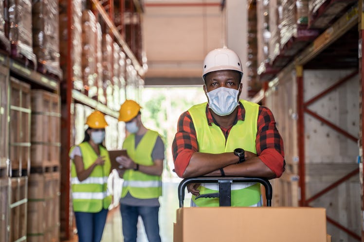 A Black male worker is wearing protective face mask and a bright yellow hazard vest while working in...