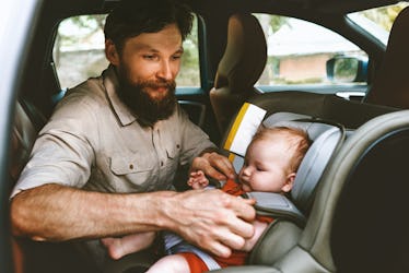 Father putting baby in safety car seat happy family vacation road trip lifestyle child care transpor...