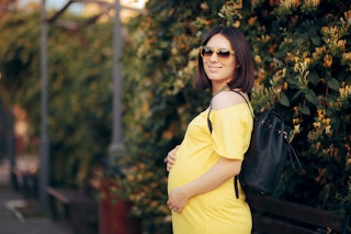 
Happy Pregnant Woman Wearing Sunglasses Carrying Backpack. Mother to be talking a walk in the park ...