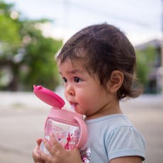 Close-up baby girl drink water from bottle via straw while go for walk outdoor.