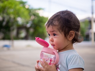 Close-up baby girl drink water from bottle via straw while go for walk outdoor.