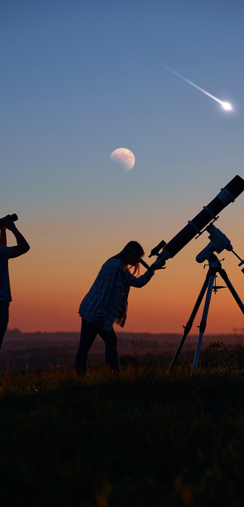 Couple stargazing together with a astronomical telescope, looking at planets, stars, lunar eclipse a...