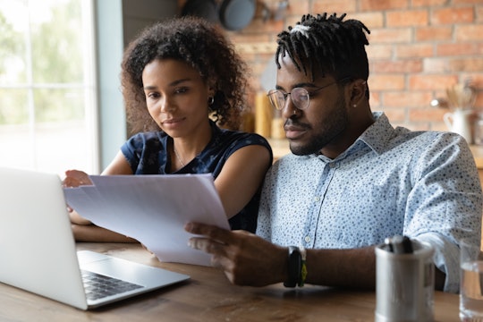 Serious millennial black married couple reading documents at laptop together, checking monthly bills...