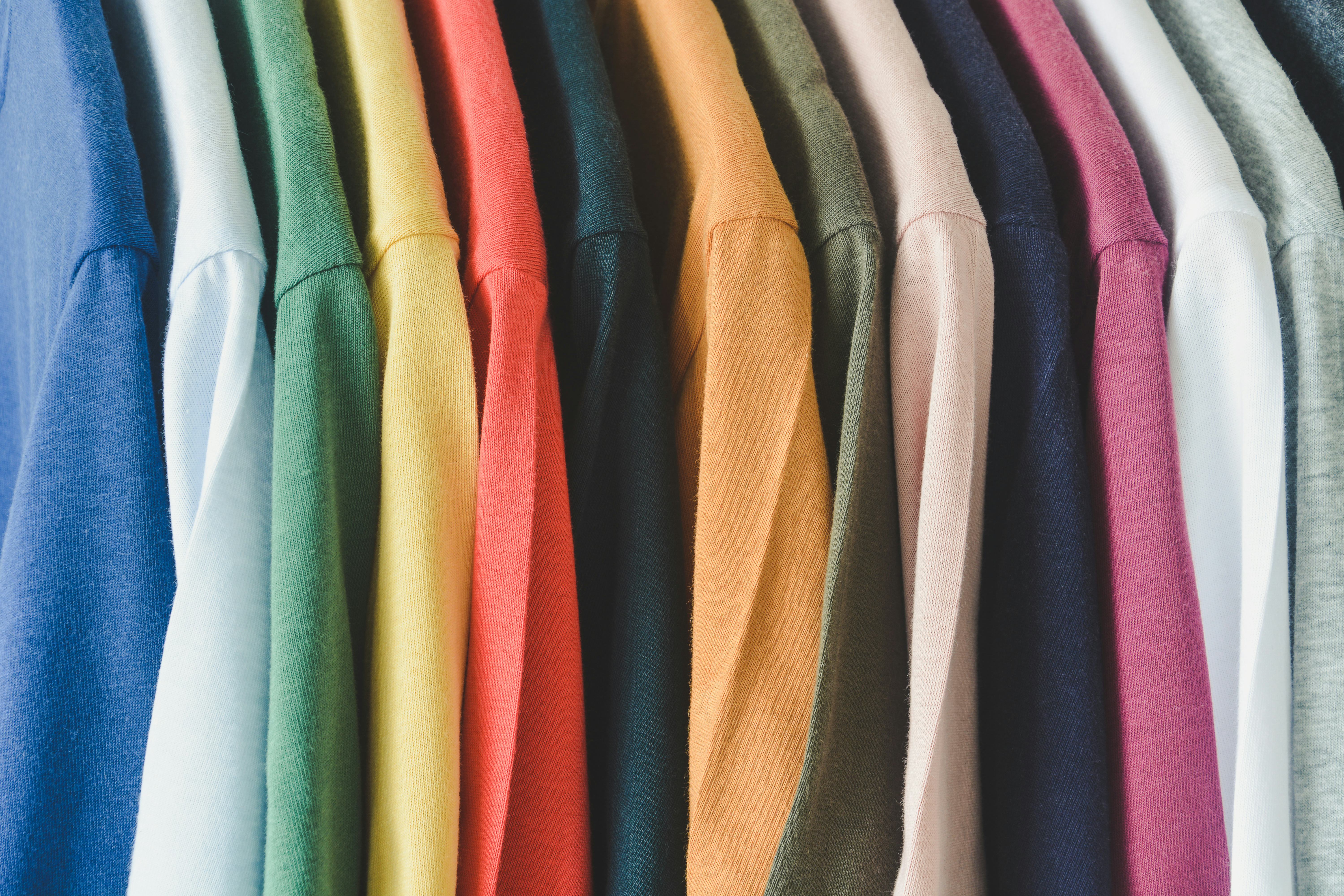 close up a collection of colorful t-shirts hanging on a clothes hanger in closet or clothing rack