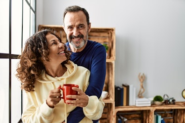 Middle age hispanic couple smiling happy and drinking coffee. Leaning on the window at home.