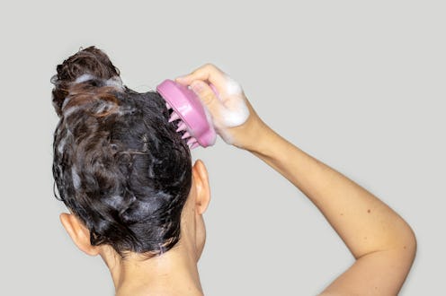 hair growth stimulating, scalp massage.woman using pink scalp massager shampoo brush with silicone,...