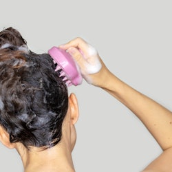 hair growth stimulating, scalp massage.woman using  pink scalp massager shampoo brush with silicone,...