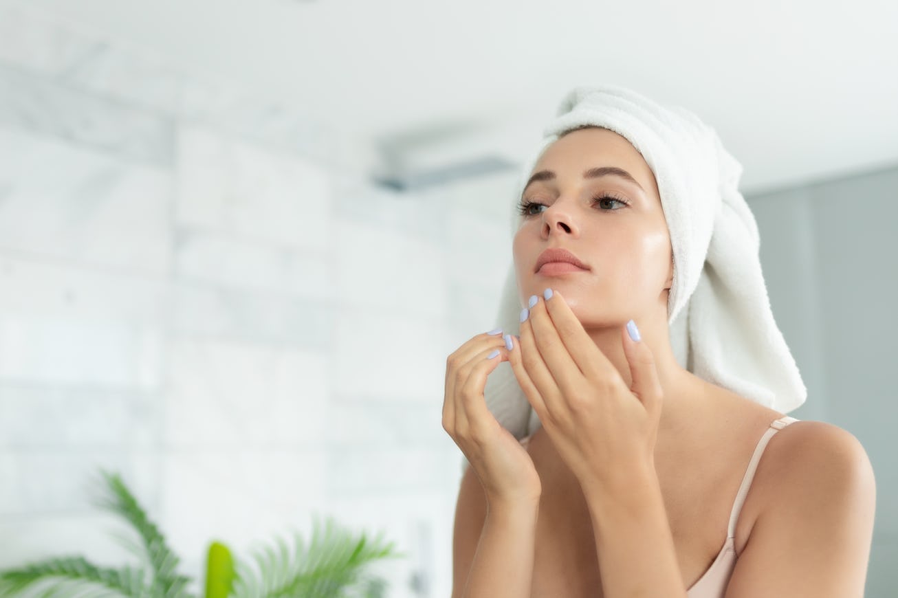Young beautiful woman wearing bath towel and underwear standing in bathroom and looking for or squee...