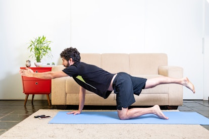 A man at home on blue yoga mat doing bird-dog pose.