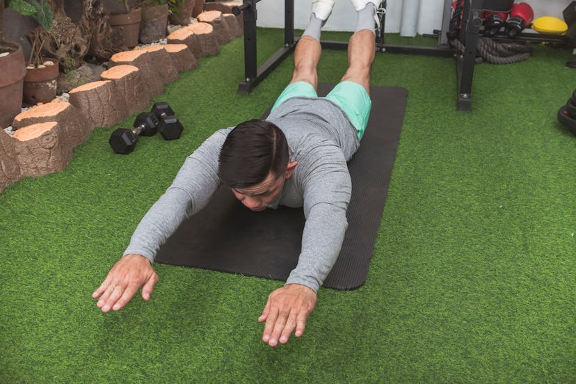 A man does Superman Back Extensions on a black mat, lying on his stomach and lifting his arms, chest...