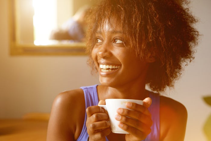 Close up portrait of a smiling young african american woman with coffee cup in an article about inst...