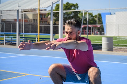 A man does jump squats on a tennis court.
