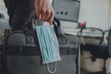 A person carries a briefcase and a surgical mask in an office