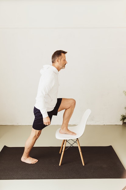 A man steps onto a chair at home while working out.