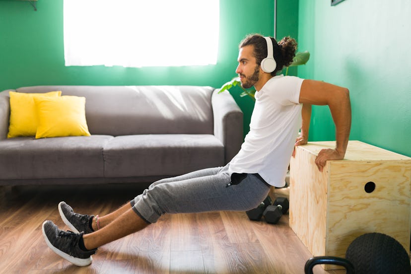 A man does tricep dips on furniture at home.