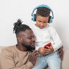 一个黑人爸爸和他的儿子在看他儿子的手机，而他的儿子戴着蓝色耳机