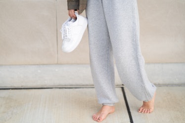 Person wearing sweatpants and holding white sneakers in one hand